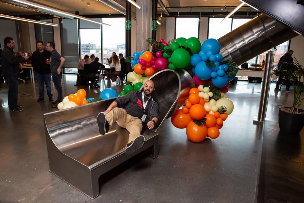 A Red Canary employee goes down a slide surrounded by colorful balloons 